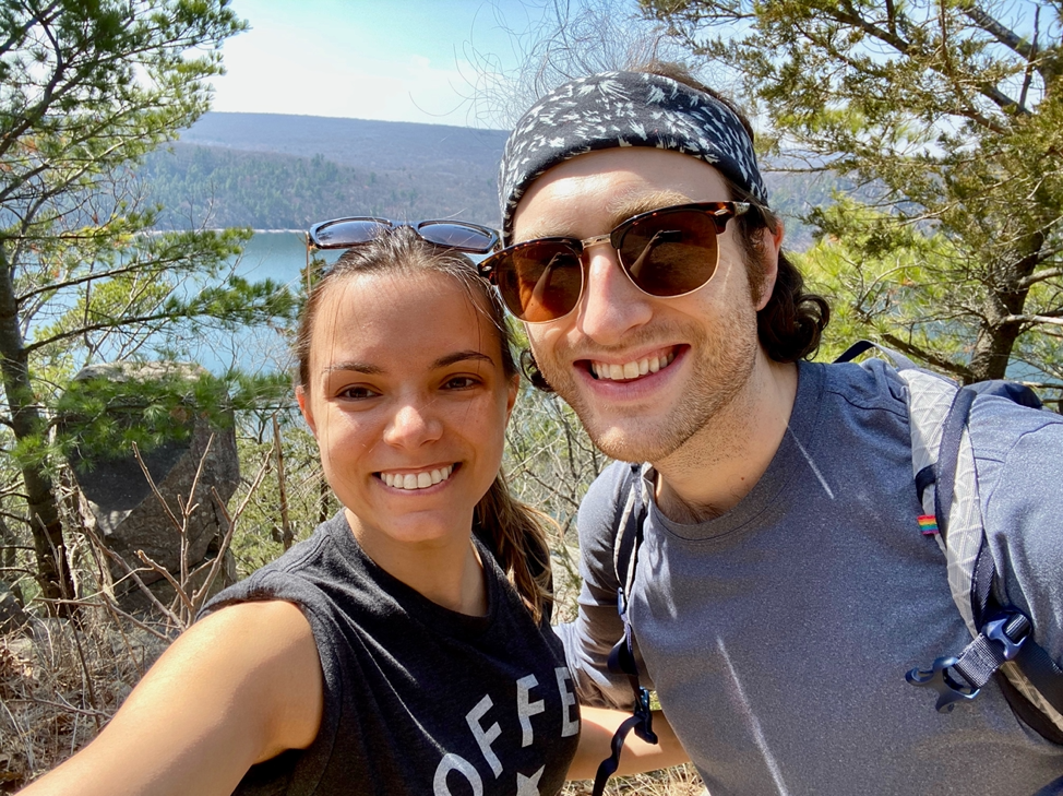 Dr. Aidanne with her husband out hiking with trees and a lake behind them