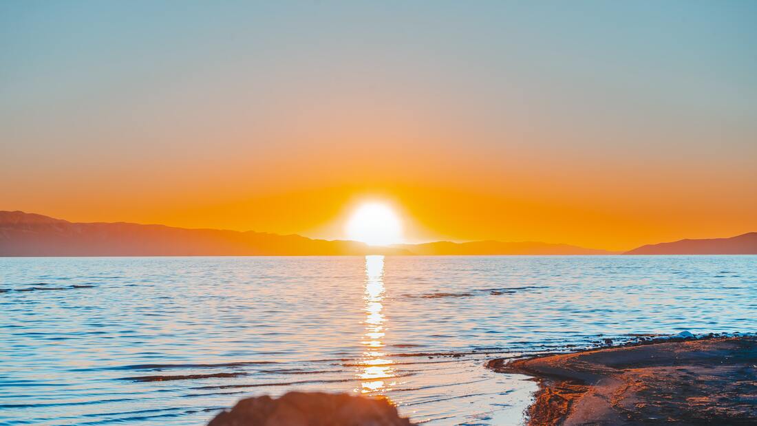 Sun setting over a body of water with an orange sky and mountainous scenary
