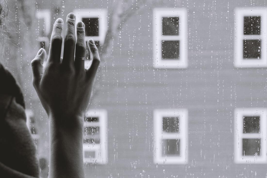 Black and white photo of someone's hand on a window that is streaked with raindrops